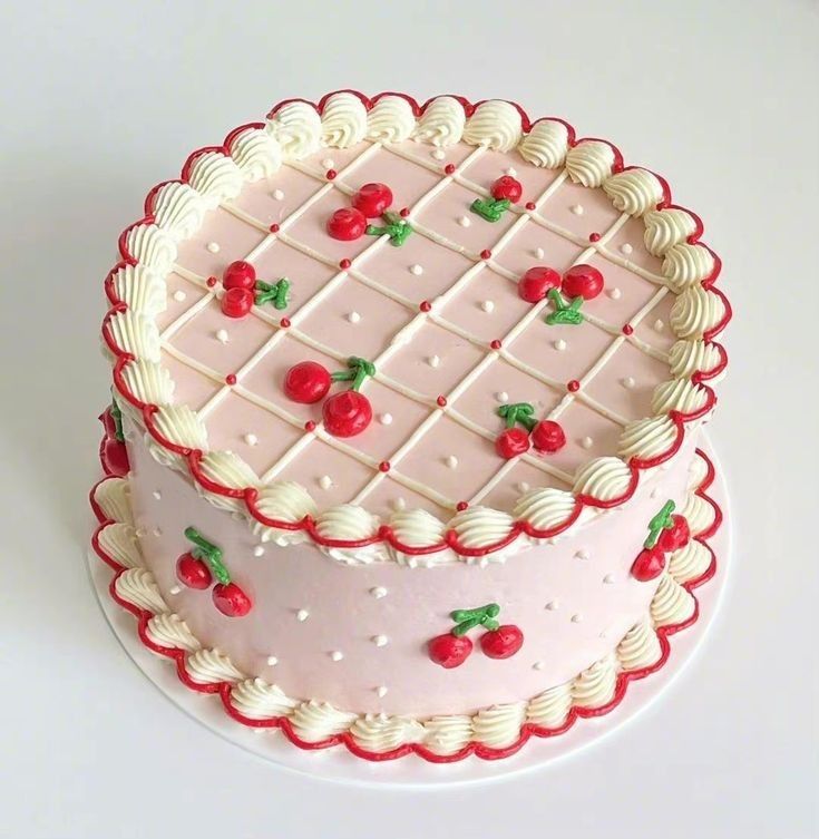 Vintage-inspired round pink cake with white quilted buttercream lattice, red piped cherries, and ornate shell borders on a white background.