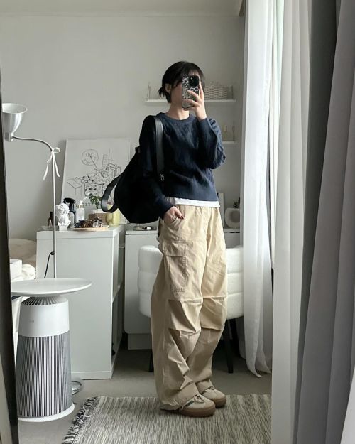 A Korean university student wearing a navy blue cable knit sweater with a white undershirt, baggy tan cargo pants, and a black backpack.