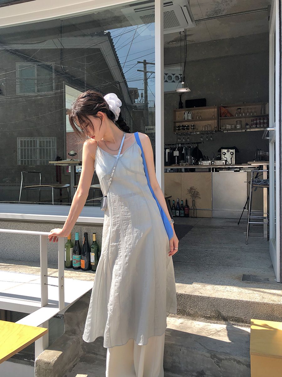 A woman standing in front of a cafe wearing a sheer light green midi slip dress layered over wide-leg cream trousers, styled with a blue tote bag and a white hair scrunchie.