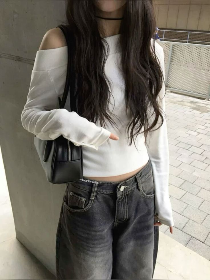 A woman wearing a white off-the-shoulder long-sleeve crop top paired with faded grey wide-leg jeans and a black shoulder bag.