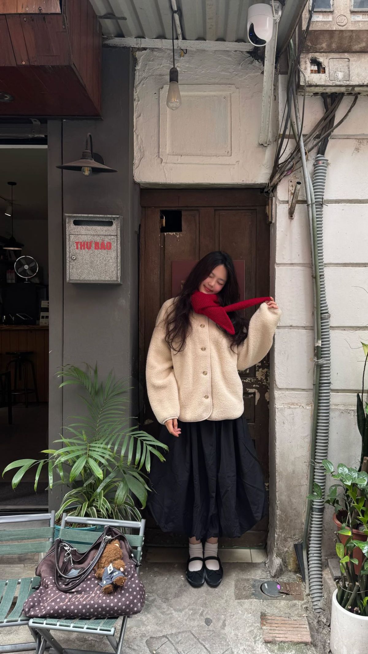 A woman is wearing a fuzzy cream jacket, a flowing black skirt, a red scarf, and black shoes.