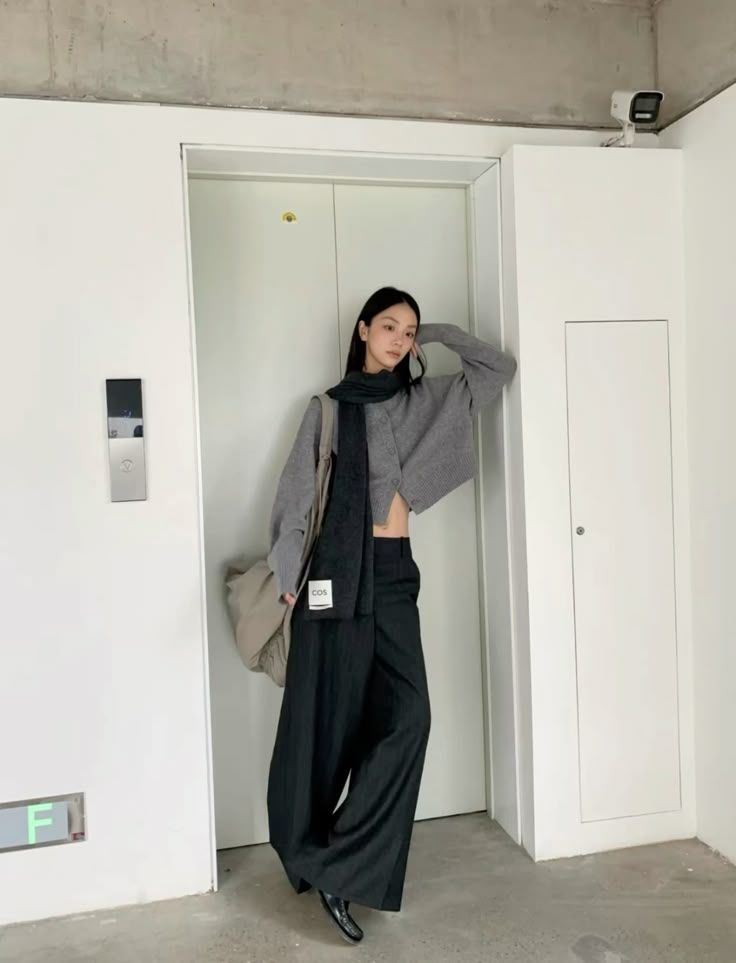 The outfit features a cropped gray knit sweater, wide-leg black trousers, and a long black scarf.