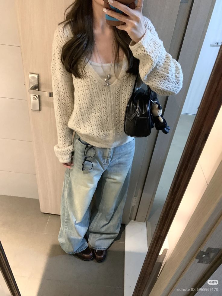 The outfit features a cream cable knit sweater layered over a white tank top, paired with light blue baggy jeans and brown loafers.
