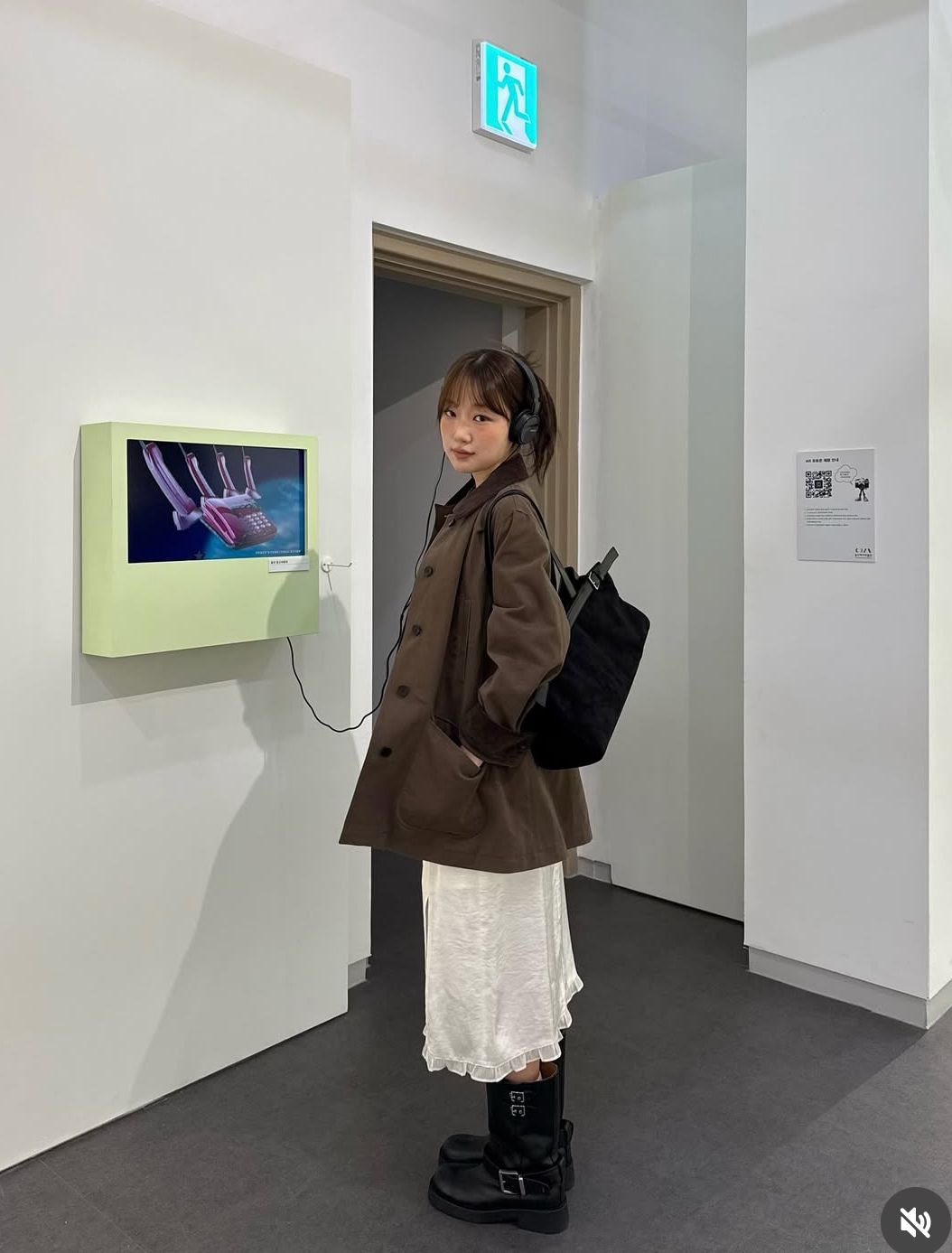 The outfit features an oversized brown coat, a white slip dress, and black ankle boots.