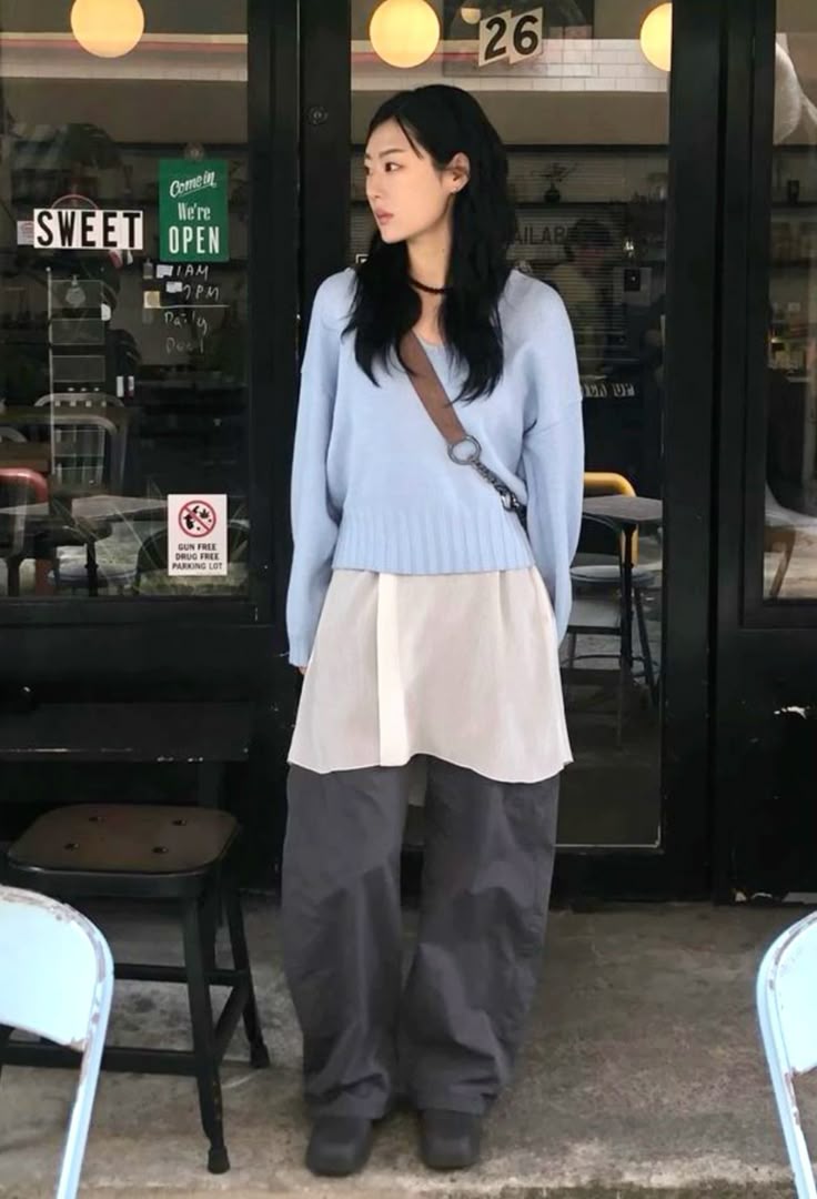 A light blue sweater paired with a layered oversized shirt dress and baggy gray pants.