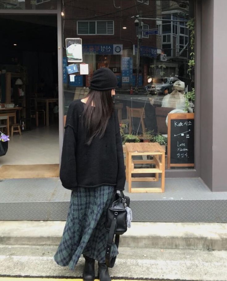 An oversized black sweater paired with a plaid maxi skirt in shades of green and black, completed with a beanie and ankle boots.