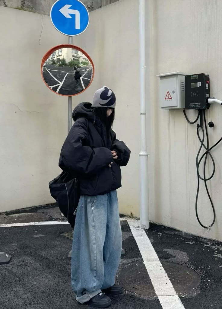 The outfit features a black puffer jacket, light blue baggy denim pants, and a patterned beanie.