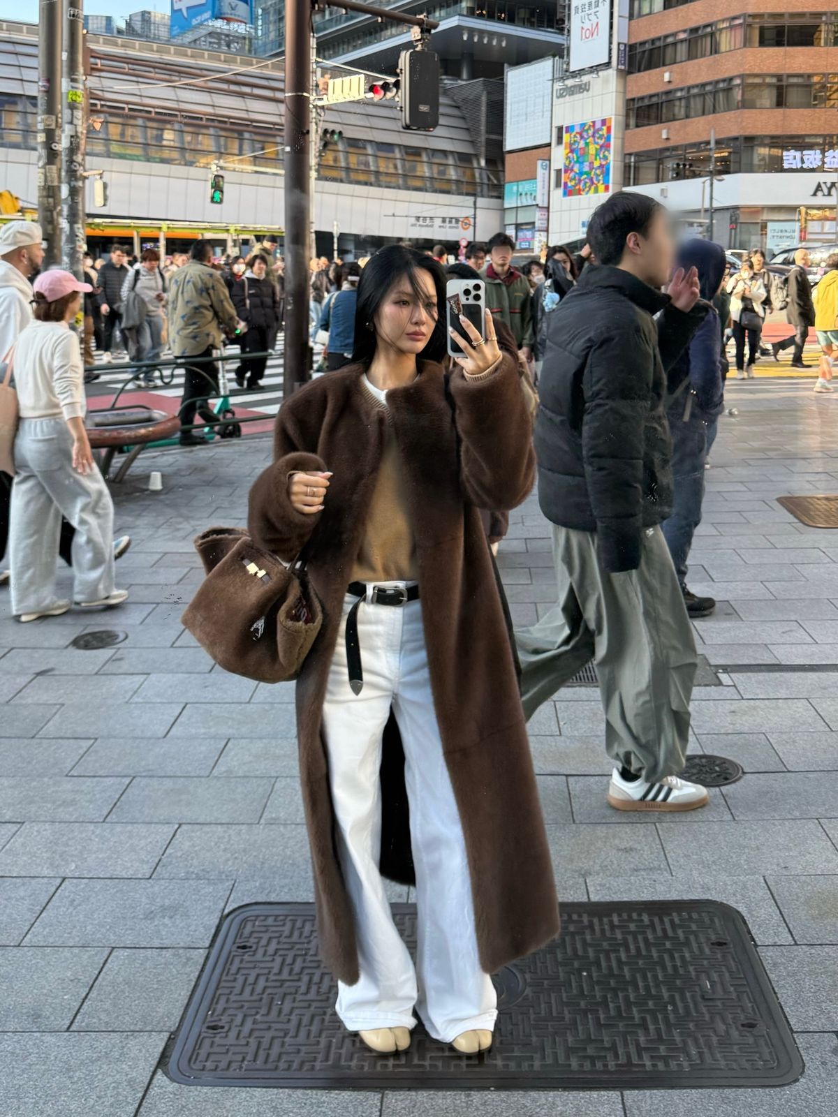 The outfit features a brown oversized coat, a beige top, and white wide-leg pants.