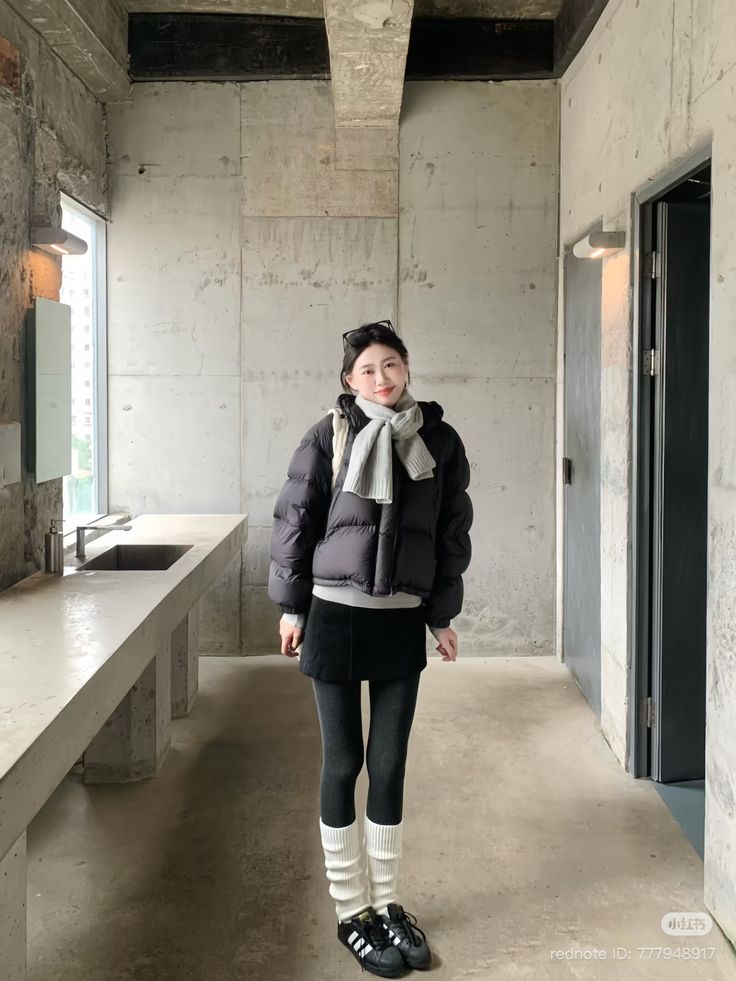 The outfit features a black puffer jacket, a gray sweater, a black mini skirt, gray leggings, and white knee-high socks.