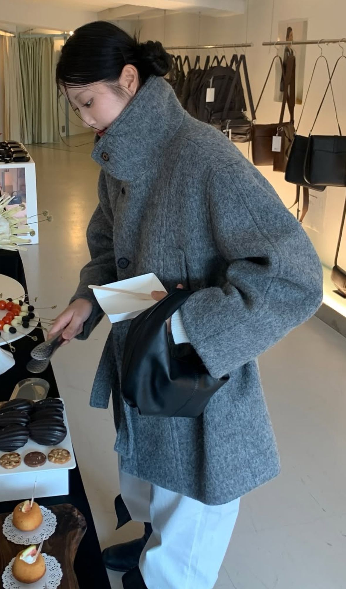 The outfit features an oversized gray coat, wide leg trousers, and a black handbag.