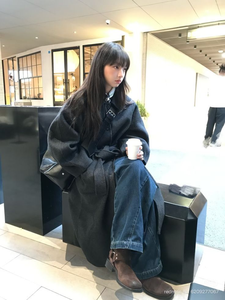 The outfit features an oversized gray coat, wide leg blue jeans, and brown ankle boots.