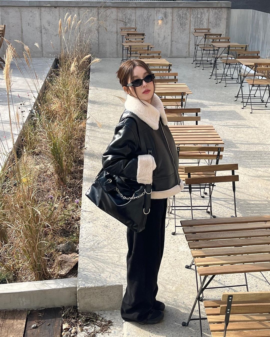 An outfit featuring a black shearling jacket, wide leg black pants, and black sunglasses.