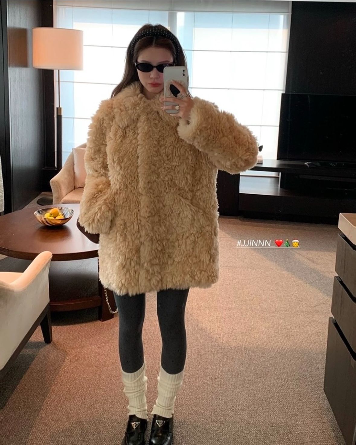 The outfit features a beige faux fur coat, dark leggings, and white knitted leg warmers.