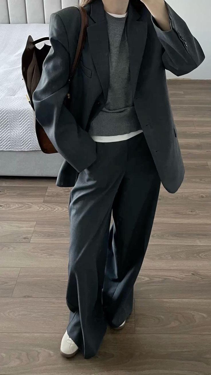 The outfit features an oversized blazer, a gray sweater, and wide leg trousers in a dark color.