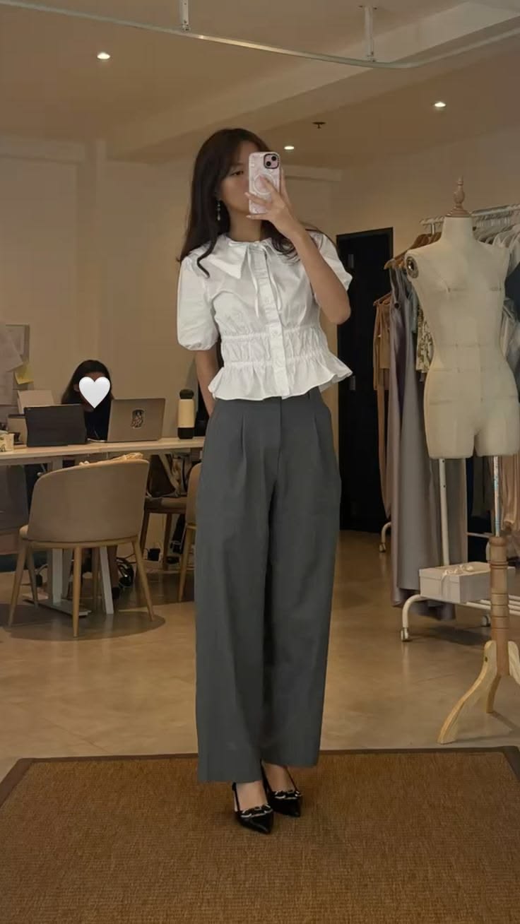 The outfit features a white peplum blouse and gray wide leg trousers paired with black heels.