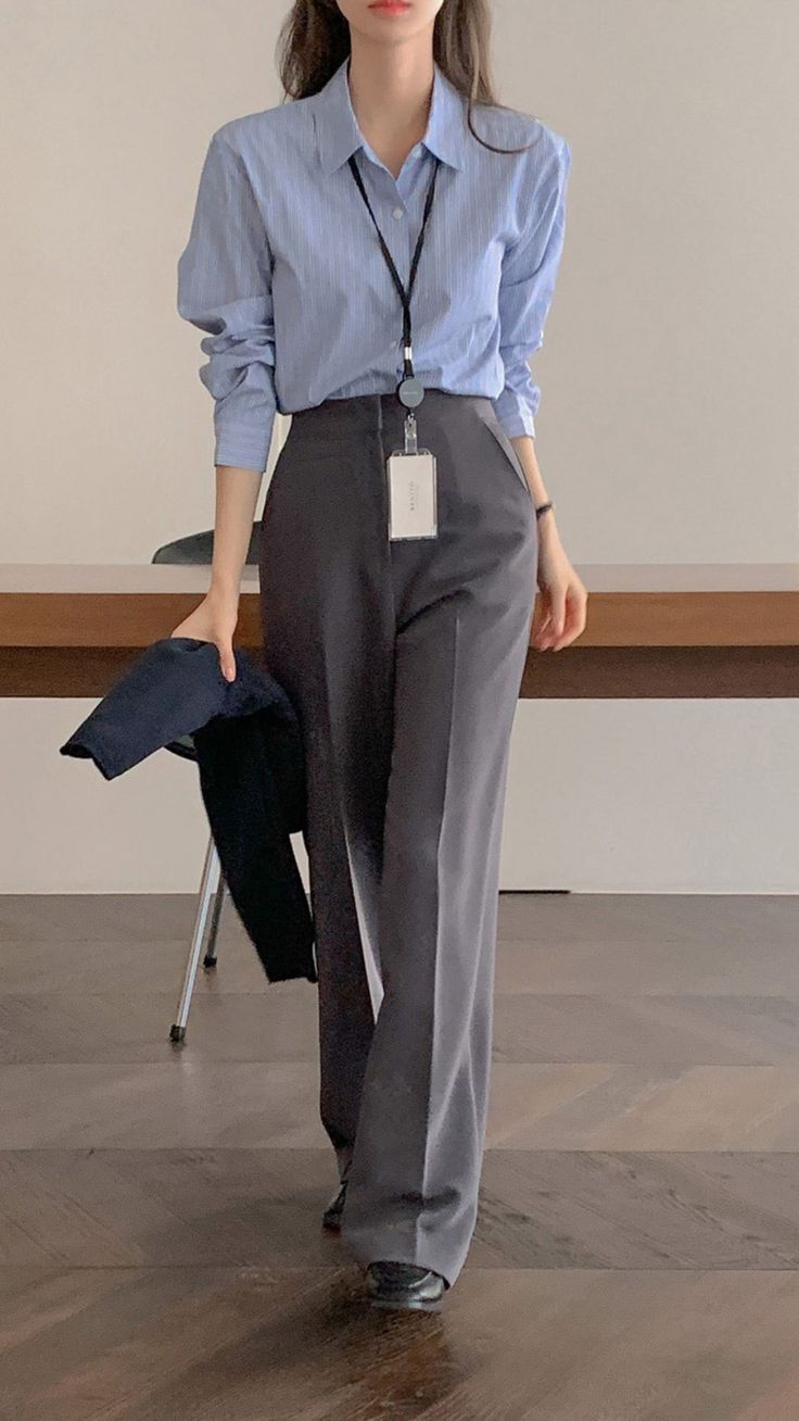 A woman wearing a striped blue button-up shirt, wide-leg gray trousers, and black shoes.