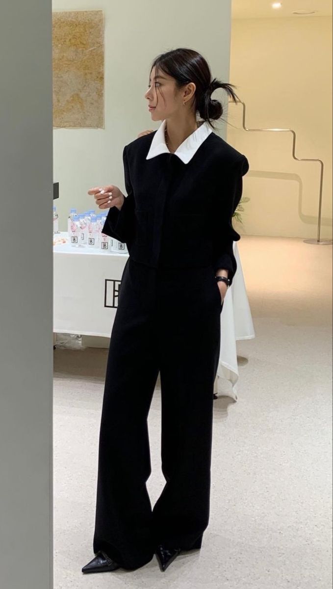 The outfit features a black jumpsuit with a white collar shirt and pointed black shoes.