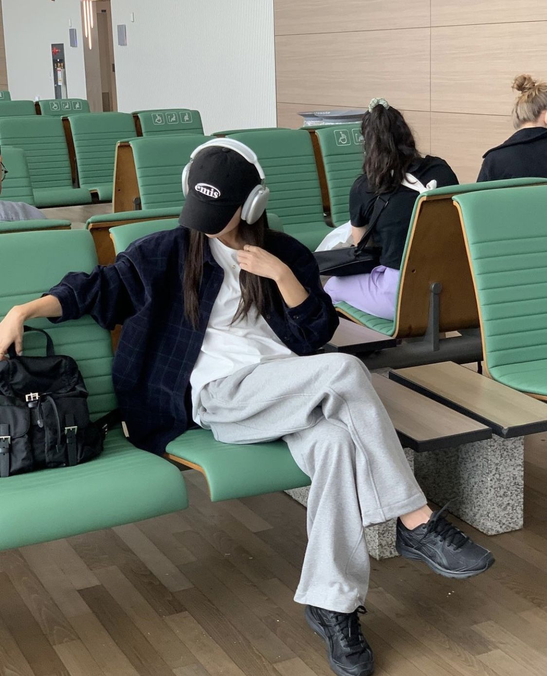 The outfit features a plaid overshirt, a white t-shirt, grey sweatpants, and black sneakers.