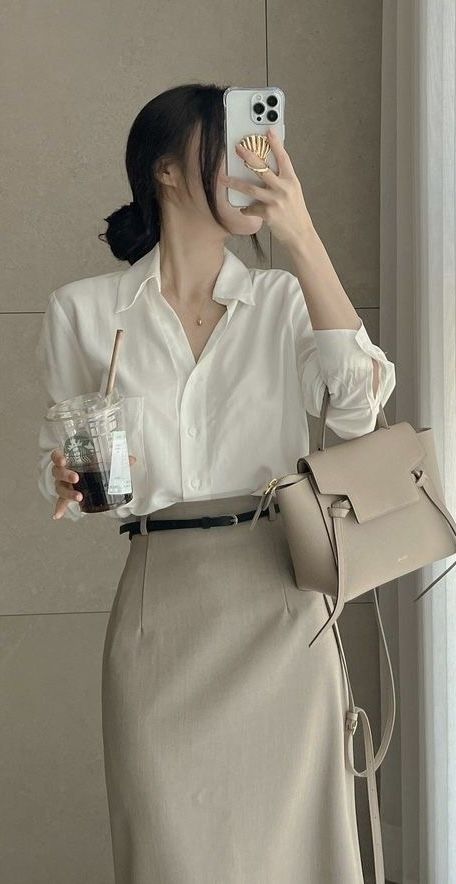 The outfit features a white button-up shirt and a beige pencil skirt, complemented by a black belt and a light beige handbag.