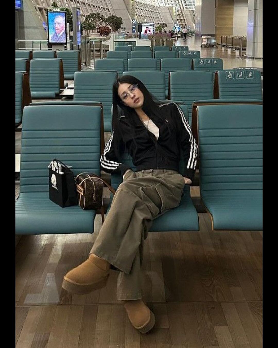 Outfit features a black zip-up track jacket with white stripes, baggy olive cargo pants, and tan boots.