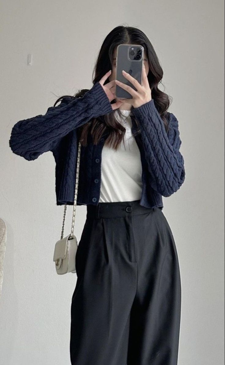 A navy knitted cardigan layered over a white top, paired with black wide leg trousers and a small handbag.
