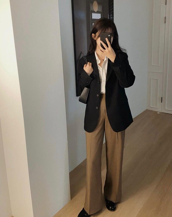 A black blazer paired with wide leg brown trousers and a white shirt, complemented by a small black bag.