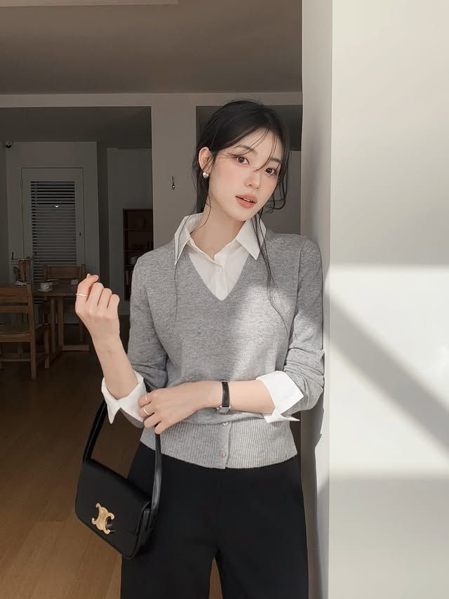 A gray v-neck sweater layered over a white shirt, paired with black wide leg trousers and a small black bag.