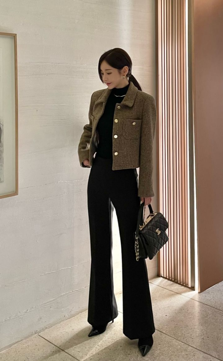 The outfit features a brown tweed jacket, a black turtleneck, and black flared trousers.