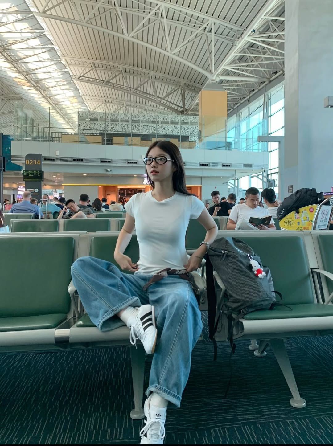 The outfit features a fitted white t-shirt paired with loose, light blue denim jeans and white sneakers.