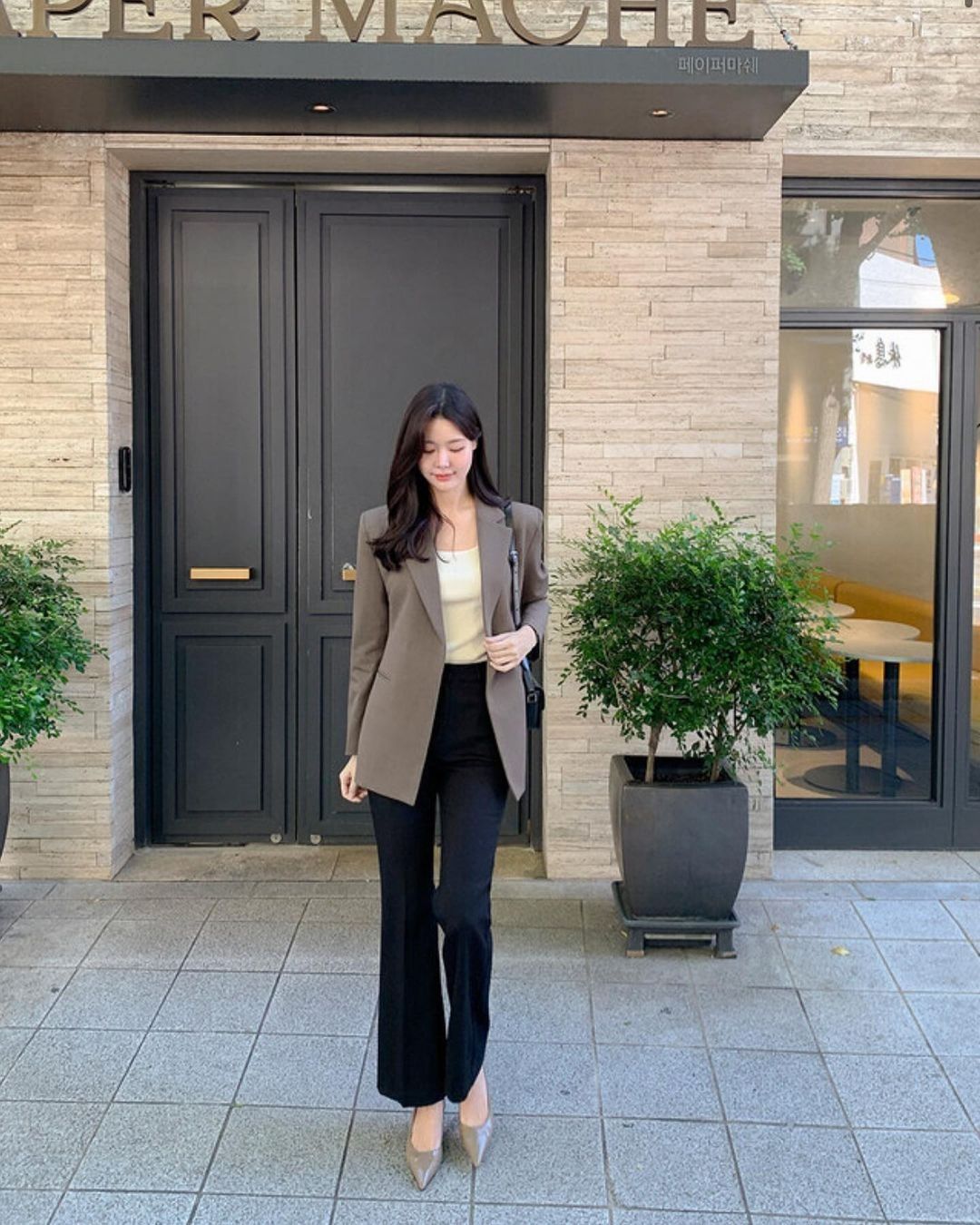 A woman wearing a brown blazer, cream top, and black flared trousers, paired with nude heels.