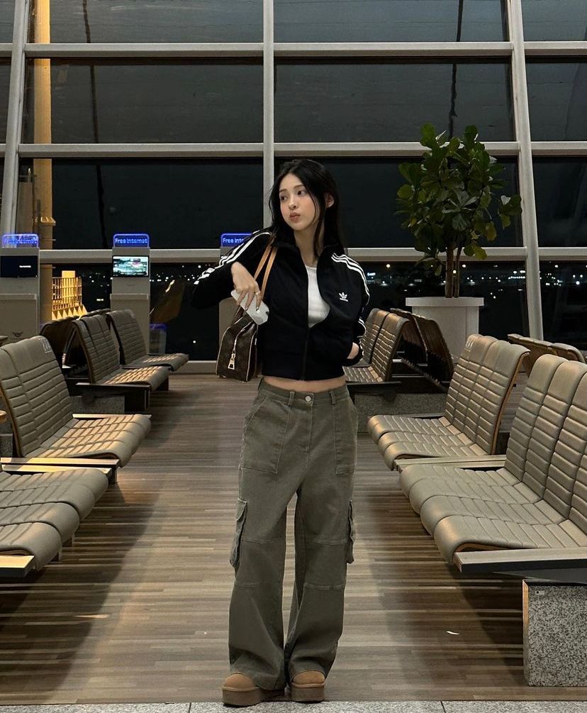 A woman wears a black zip-up jacket, white crop top, and olive green baggy cargo pants with brown platform shoes.